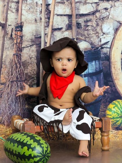 This little cowboy has a look of surprise. The rustic set with hay and a wagon wheel provides the perfect backdrop for a wild west story.