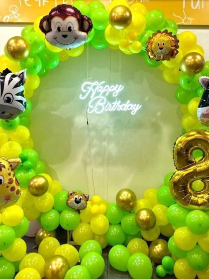 A jungle-themed balloon ring using bright green and yellow balloons. The ring is decorated with various animal head foil balloons like a monkey, zebra, and lion, perfect for a child's 8th birthday.