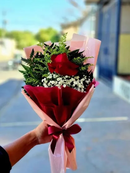 A single red rose bouquet, elegantly arranged with fresh ferns and baby's breath. The deep red and pink wrapping makes this a simple but passionate statement.