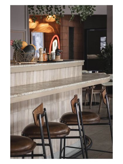 A detail of the bar seating, featuring industrial-style stools with leather seats. These material choices add to the sophisticated yet relaxed character of the restobar.