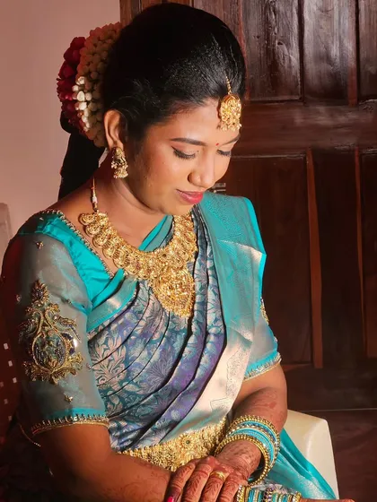 A side profile of a bride in a blue silk saree, showing her elegant hairstyle and the beautiful details of her makeup.