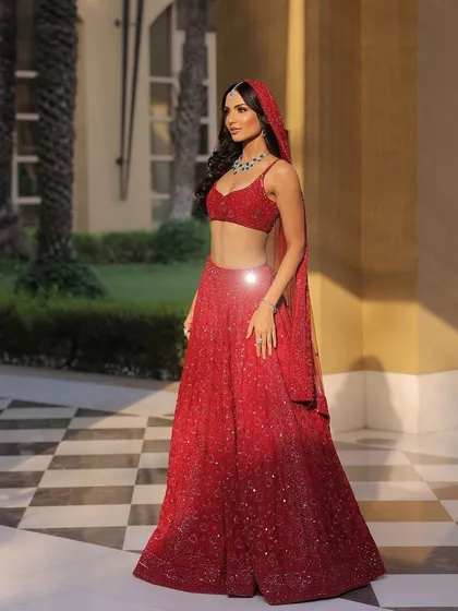 A full-length shot capturing the sleek and modern silhouette of this red lehenga against a chic checkered floor.