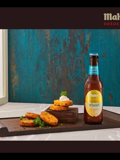 A focused shot of the Mahou Wheat bottle with stacked vegetable cutlets. The composition uses height and texture to draw the eye and present the product in a sophisticated manner.