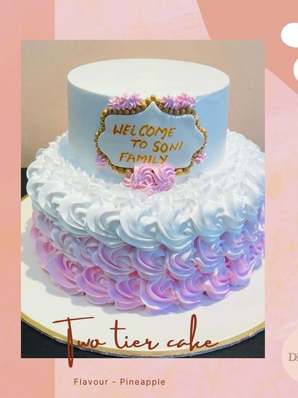 A charming two-tier welcome cake with a pink and white ombre rosette design. The custom plaque makes it a perfect centerpiece for welcoming a new family member.