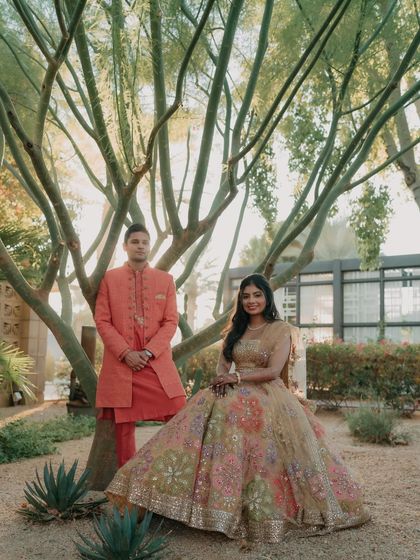 A classic, elegant portrait from an Arizona wedding. The couple stands together against a tree, their colorful outfits complementing the beautiful desert garden setting.
