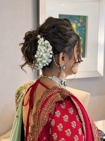 A detailed view of a traditional bridal updo, intricately woven and adorned with fresh jasmine flowers, or gajra. This classic hairstyle is perfect for wedding ceremonies, offering a timeless elegance that complements traditional Indian bridal wear.