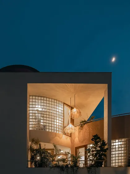 As dusk falls, the home reveals a different kind of beauty. The warm interior light glows through the glass block walls and open balconies, transforming the structure into a welcoming beacon against the night sky.