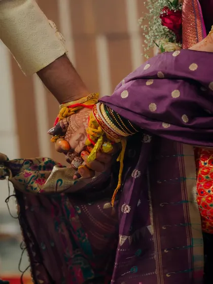 A close-up shot of the couple holding hands during the ceremony. This image focuses on the connected hands, adorned with turmeric and sacred threads, symbolizing their union and shared path forward.
