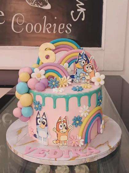 A cheerful Bluey-themed cake with rainbows, flowers, and a pastel drip effect. It's a fun and colorful design that brings the beloved cartoon to life.