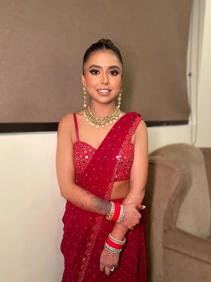 A full shot of the classic red saree and smokey eye combination. The makeup is designed to be bold and make a statement.
