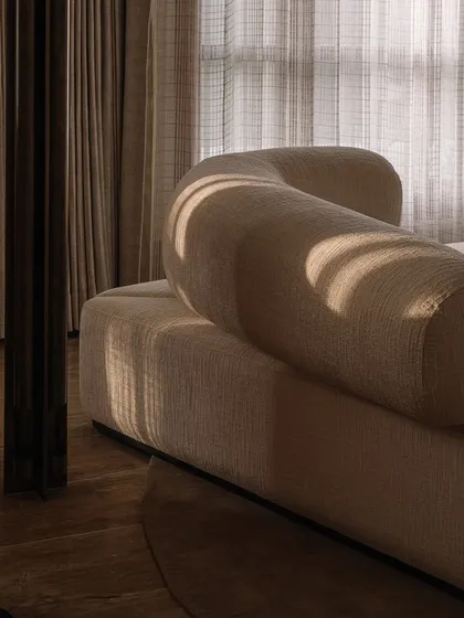 The play of light and shadow on the curved, upholstered forms of this custom sofa highlights its sculptural quality. We focus on creating furniture with soft, inviting silhouettes that anchor a room.