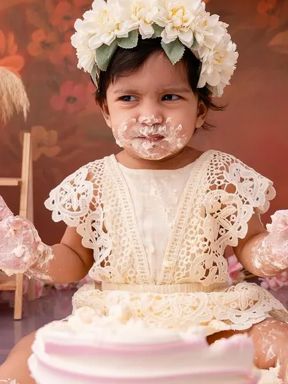 With cake on her hands and a happy expression, this little girl is fully enjoying the messy fun of her birthday cake smash.
