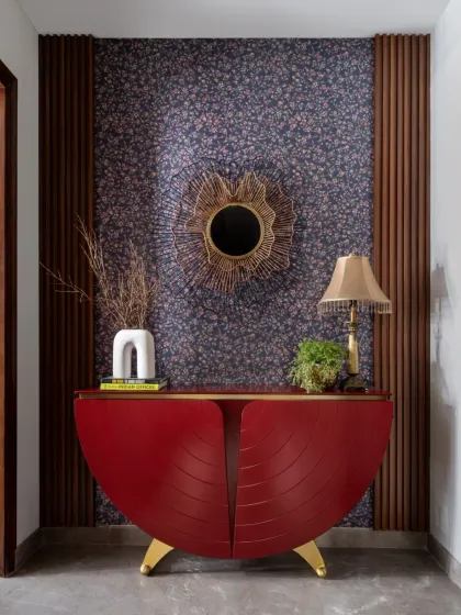 A striking first impression is made with this entryway console. The bold red, semi-circular cabinet, patterned wallpaper, and sculptural mirror create a corner that is full of personality and style.