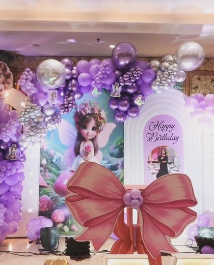 An elaborate fairy and butterfly theme for a 5th birthday, featuring multiple character cutouts, a large pink bow, and a light-up number '5' set against a backdrop of purple and silver balloons.