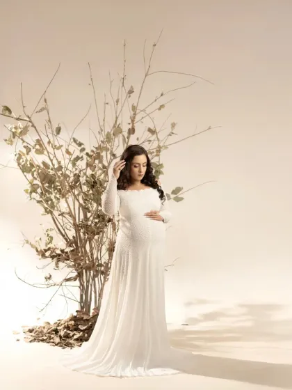 A moment of gentle reflection. This studio portrait captures the mother-to-be looking down, her hand on her hair, in a soft and thoughtful pose that highlights her serene beauty.