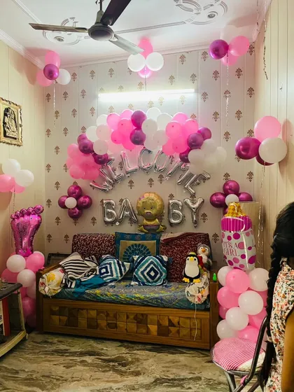 A cozy corner transformed for a baby's welcome. This setup includes "Welcome Baby" foil balloons, a cute lion balloon, and pillars of pink balloons with a baby foot and feeding bottle design.