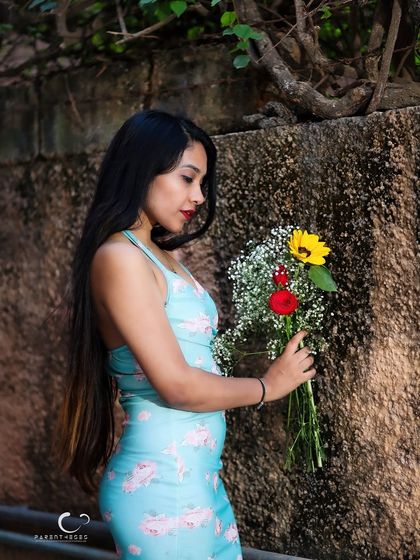 A profile shot against a textured stone wall. The contrast between the soft flowers, her delicate dress, and the rough wall is visually compelling.
