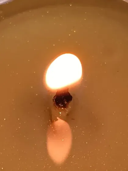 A macro shot of a lit peach-scented candle. The warm glow and the reflection of the flame in the melted wax pool create a feeling of deep relaxation.