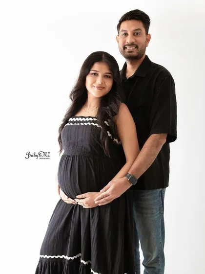 A classic and elegant maternity portrait. The coordinated black outfits create a timeless look against the simple white background.
