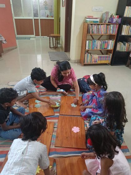 A group of children works together on their flower garlands, chatting and creating side-by-side.