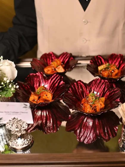 A server presents a tray of Asian-style cottage cheese appetizers in vibrant red flower-shaped bowls.