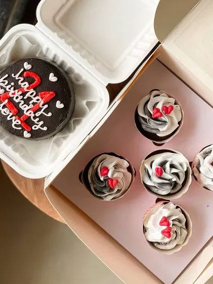 A full view of the 21st birthday combo, featuring a dark chocolate bento cake and a box of five coordinated cupcakes with black and white frosting and red hearts.