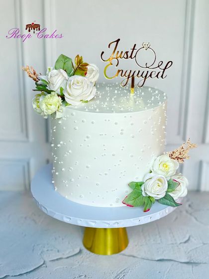 Forever starts now. This simple and elegant all-white engagement cake is adorned with white roses and a 'Just Engaged' topper, proving that beauty lies in simplicity.