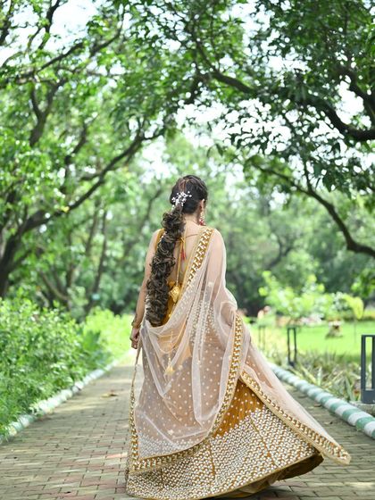 A walking shot from the back, showing the movement of the mustard yellow lehenga and its beautifully embroidered dupatta.