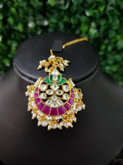 A vibrant maang tikka with a pink crescent design and kundan stones, perfect for adding a pop of color.