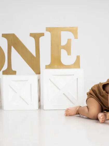 Marking the journey to one year old with a pre-birthday milestone shoot. This photo captures a baby on the move, crawling past large "ONE" props in a clean, minimalist setting.