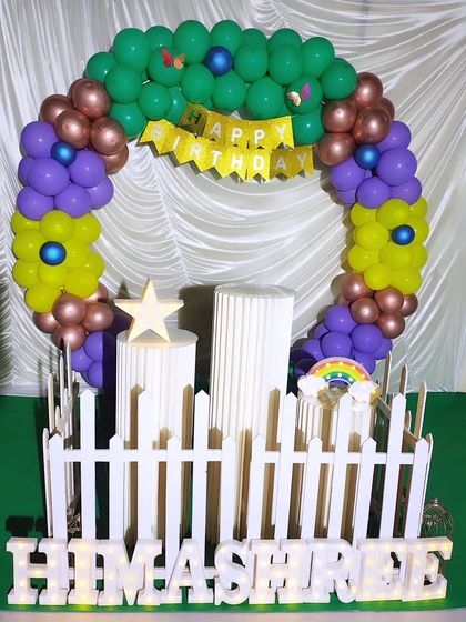 A colorful circular balloon arch with a 'Happy Birthday' banner. This setup includes pedestals and light-up marquee letters, all arranged on a green floor mat.