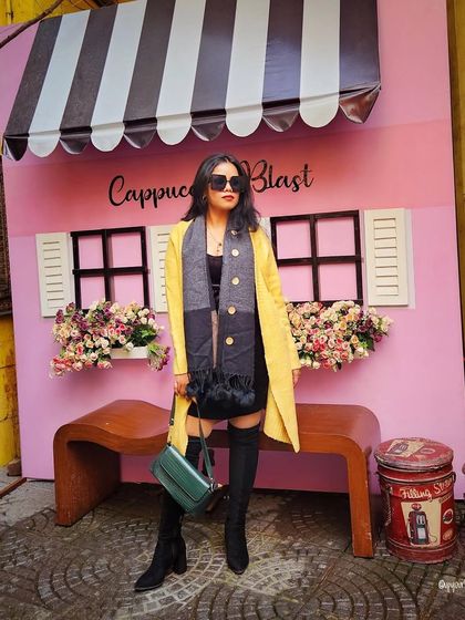 Winter workwear can be both warm and stylish. Here, a bright yellow trench coat is layered over a black dress and knee-high boots for a look that is professional and fashion-forward.