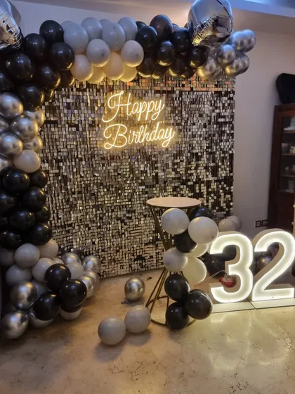 A classic black, white, and silver theme for a 32nd birthday, featuring a sequin wall, balloon arch, and marquee numbers.