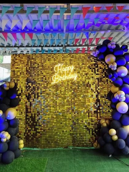 A stylish birthday backdrop with a golden sequin wall, a neon sign, and an artistic arrangement of black and yellow balloons.