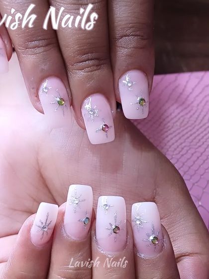 A soft, milky white set of square nails adorned with tiny, sparkling starbursts and colorful rhinestones.