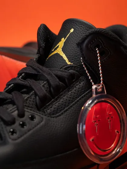Close-up on the J Balvin 'Rio' Jordan 3, focusing on the iconic smiley face hangtag and the gold Jumpman logo on the tongue.