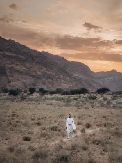 Malay stands amidst a majestic mountainscape as the golden light of sunset paints the sky. This wide shot emphasizes the grandeur of nature in a destination shoot.