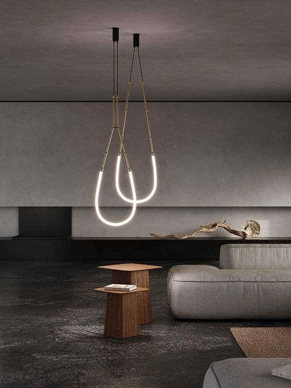 A pair of Leda pendants creates a graceful, looping sculpture of light in a dark, minimalist living room.