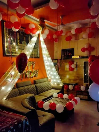 A cozy living room decoration with a canopy of lights over the sofa and red and white balloons.