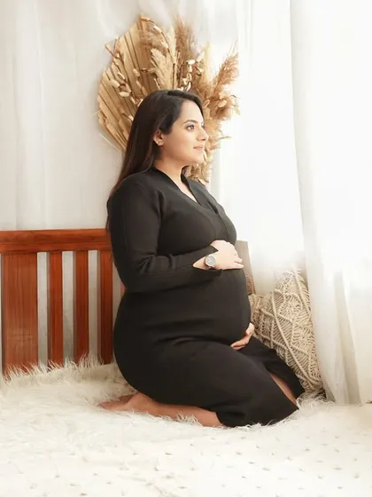A cozy and intimate bedroom setup with a simple wooden bed frame and boho decor. The mom-to-be looks peaceful and serene in a simple black dress.