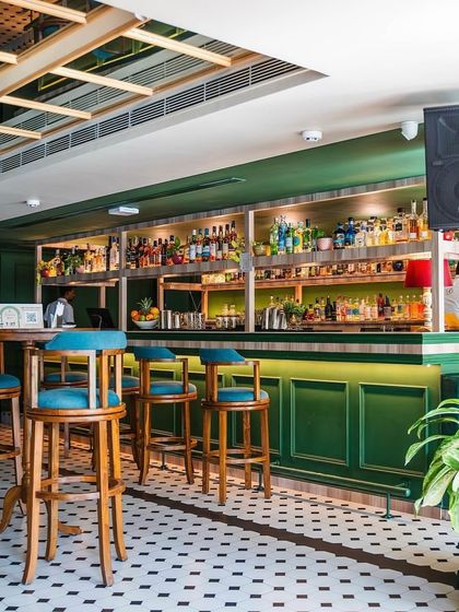 The bar area, complete with tall, solid wood bar stools with comfortable turquoise upholstered seats. These were designed to be both sturdy for a busy bar and stylish to match the overall green and white aesthetic.