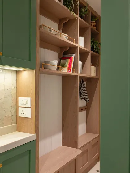 This open shelf, positioned at the kitchen entrance, is more than just storage; it’s a showcase for personality. Styled with artisanal ceramics, cookbooks, and greenery, it creates a natural transition that makes the kitchen feel open and inviting.
