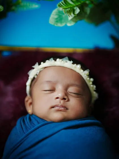 A tight portrait shot of the sleeping newborn, framed by a single green leaf, adding a touch of nature to this peaceful image.
