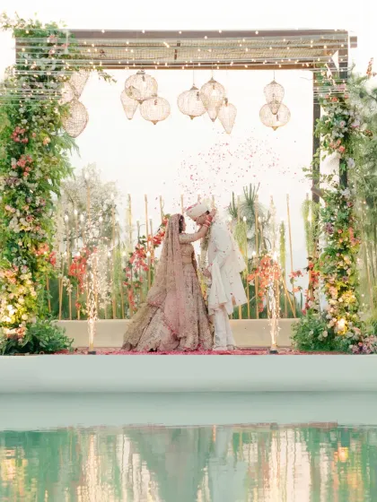 The varmala exchange by the pool at sunset. The beautiful decor and lighting create a magical atmosphere for this key wedding ritual.