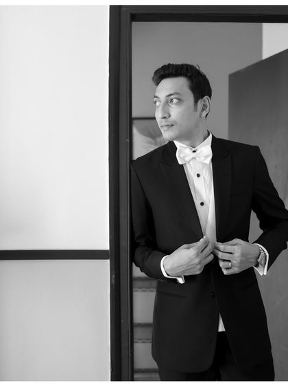A dapper groom in a classic black tuxedo and white bow tie. This black and white portrait captures a moment of anticipation, looking sharp and ready for his wedding.