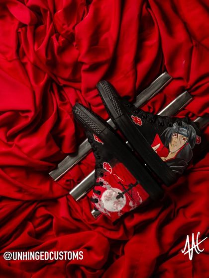 Itachi Uchiha on a pair of black Converse high-tops. This design captures the iconic, tragic scene of Itachi before the Uchiha clan massacre, set against a blood-red moon.