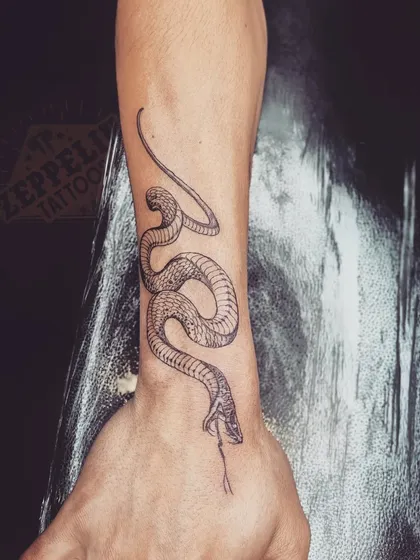 A single-needle snake tattoo designed to wrap around the wrist and hand. The fine lines allow for a high level of detail in the scales and head.