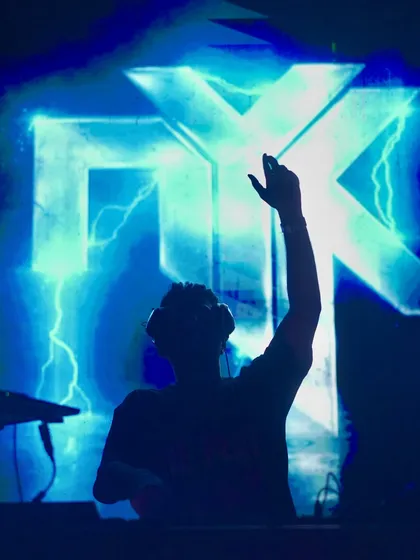 A silhouette shot of me on the decks with my signature 'NYK' logo glowing in electric blue behind me. This was taken at Xora in Hyderabad, capturing the iconic branding of my live shows.