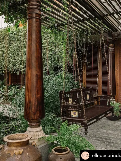 An outdoor space should be lived in and enjoyed. This traditional wooden swing, nestled among ferns and hanging vines in a Valsad home, creates a perfect, cozy corner for relaxation, seamlessly blending heritage furniture with a lush, tropical garden setting.