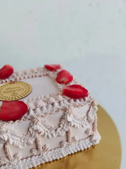 A close-up angle of the vintage anniversary cake. The combination of the pale pink frosting and red strawberries gives it a classic, romantic feel.